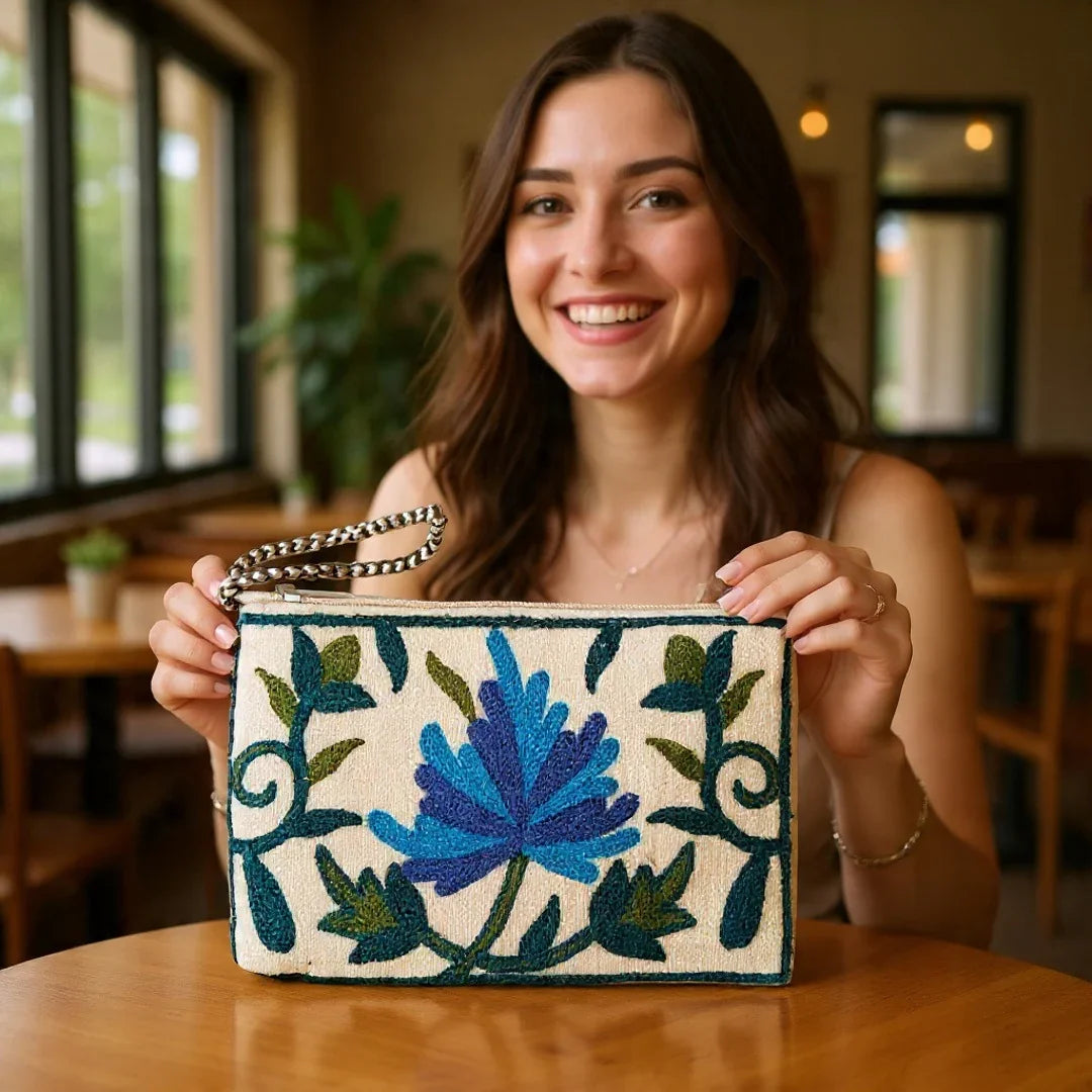 Smiling woman holding embroidered bag with blue floral design indoors at wooden table