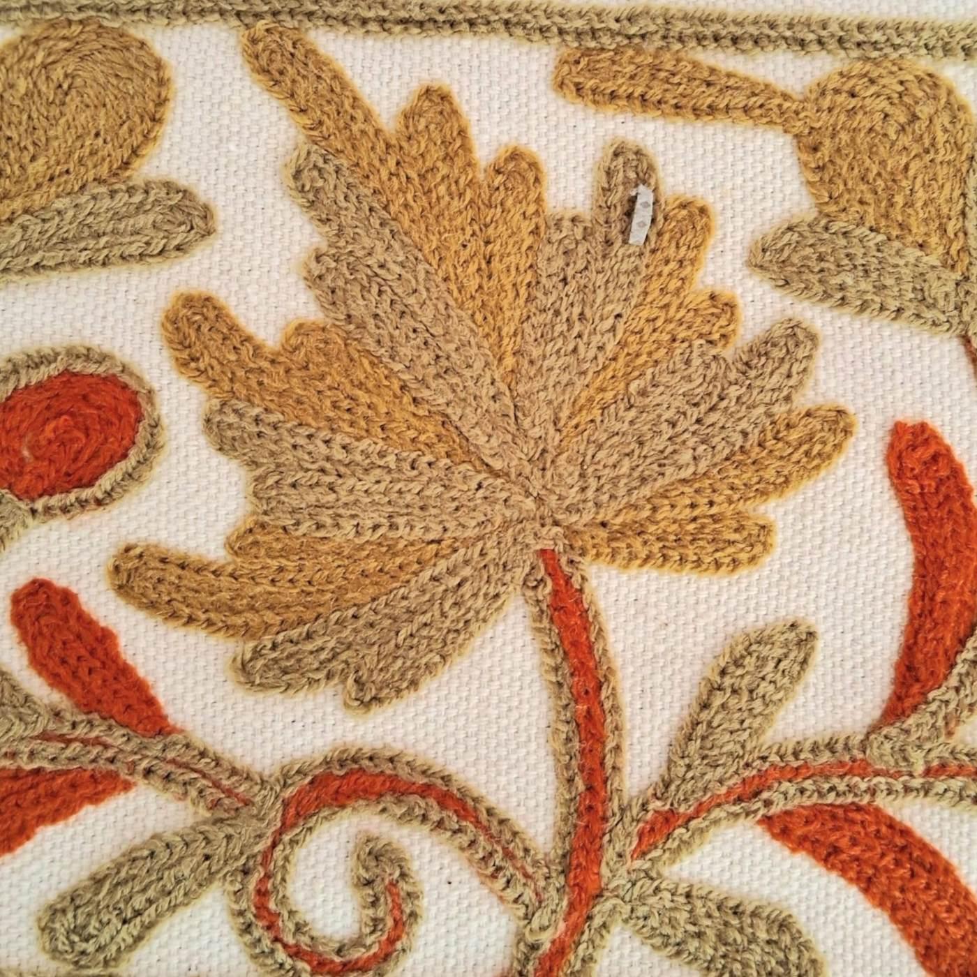 Close-up of embroidered floral design with beige, orange, and brown threads on cream fabric