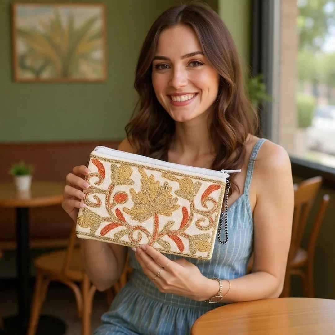 Smiling woman holding embroidered floral clutch in cafe, showcasing Zanskar Arts handcrafted accessories