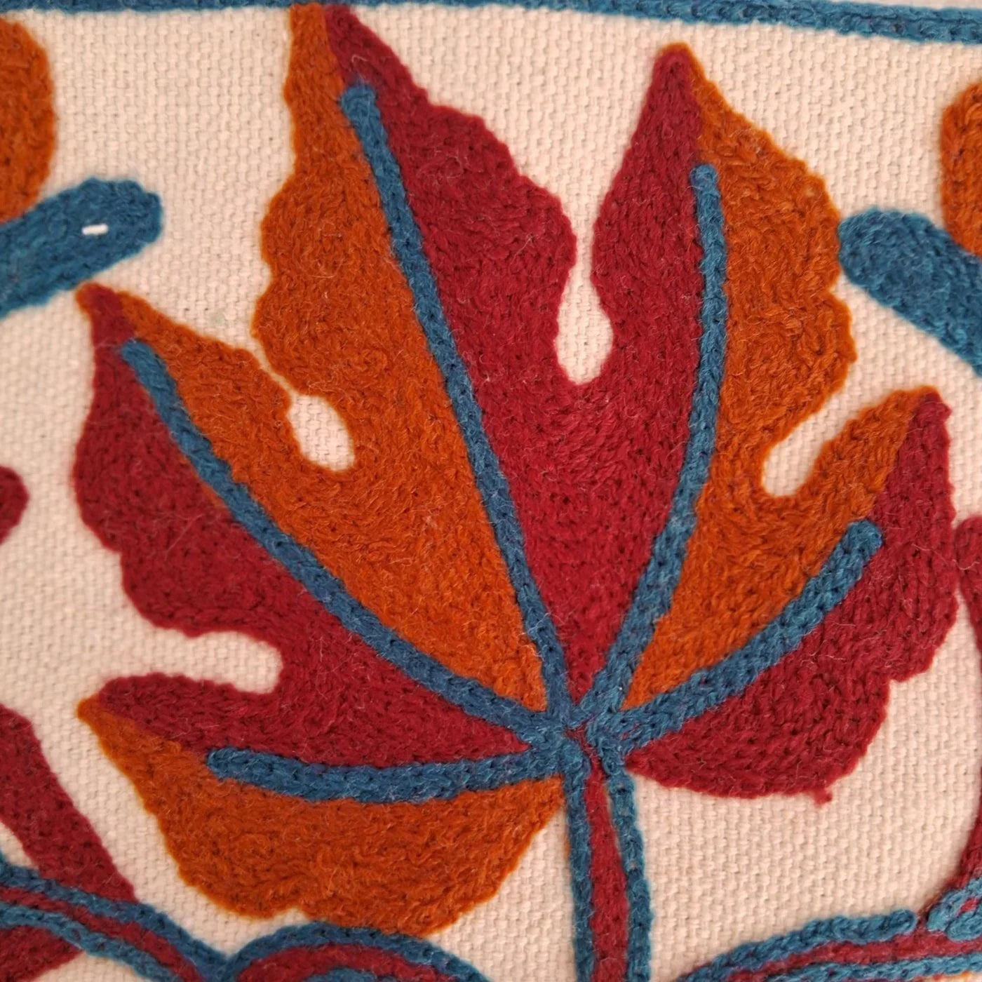 Close-up of wool embroidery with red and orange leaf pattern outlined in blue on white fabric, Zanskar Arts