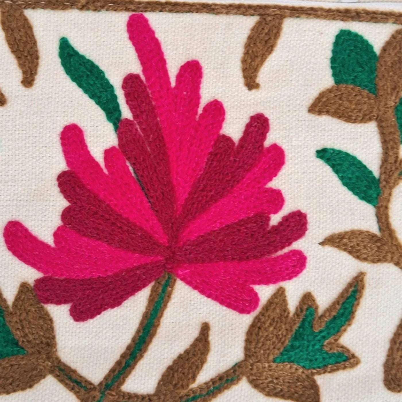 Close-up of vibrant pink and maroon floral embroidery with green leaves on cream fabric