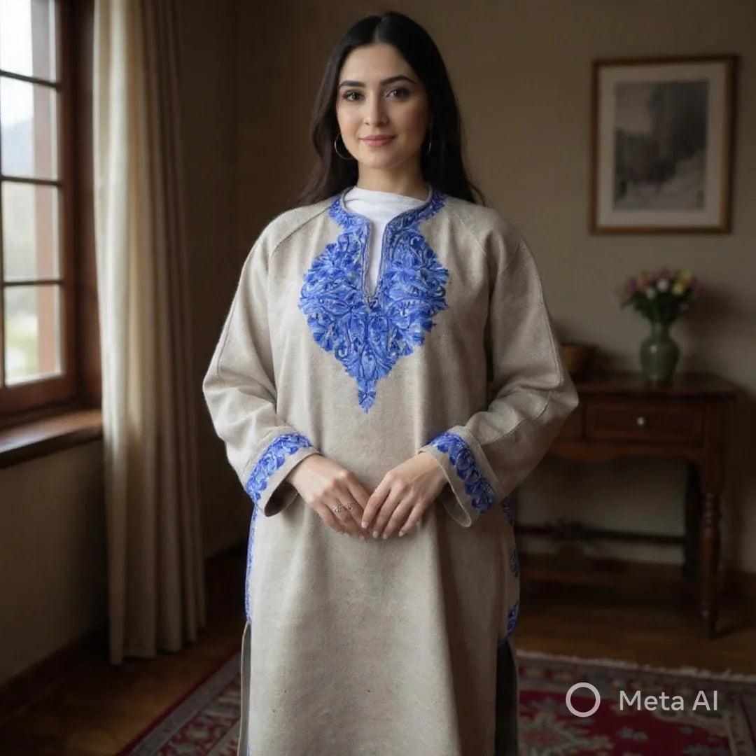 Woman wearing beige Pashmina shawl dress with intricate blue embroidery inside a cozy room with a window