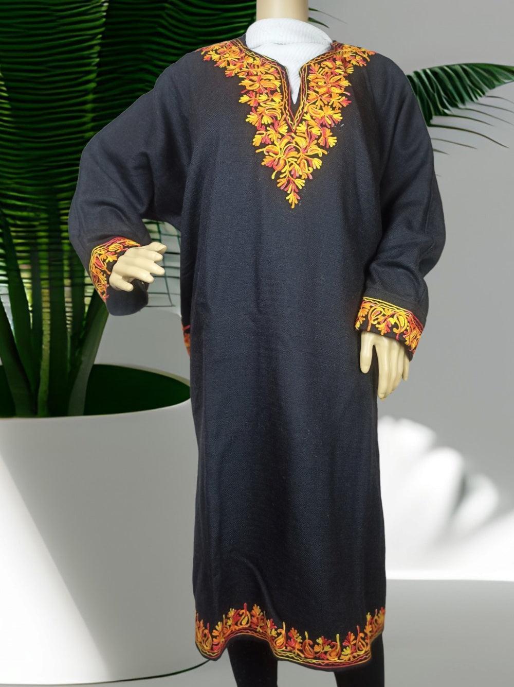 Mannequin wearing a black traditional pashmina dress with detailed orange and yellow embroidery on neckline, cuffs, and hem, displayed indoors with green plant background