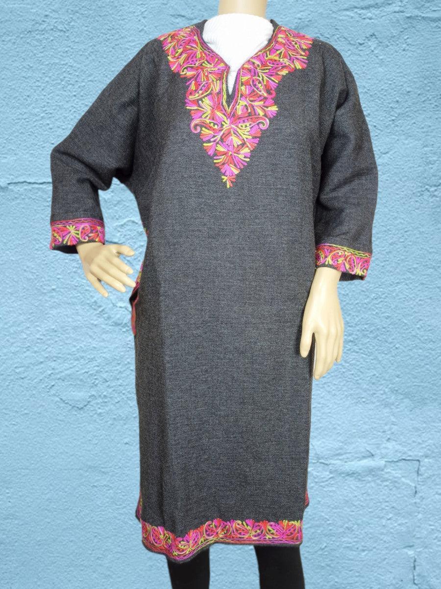 Dark grey traditional wool dress with vibrant pink and yellow floral embroidery on neckline, cuffs, and hem, displayed on mannequin against blue wall