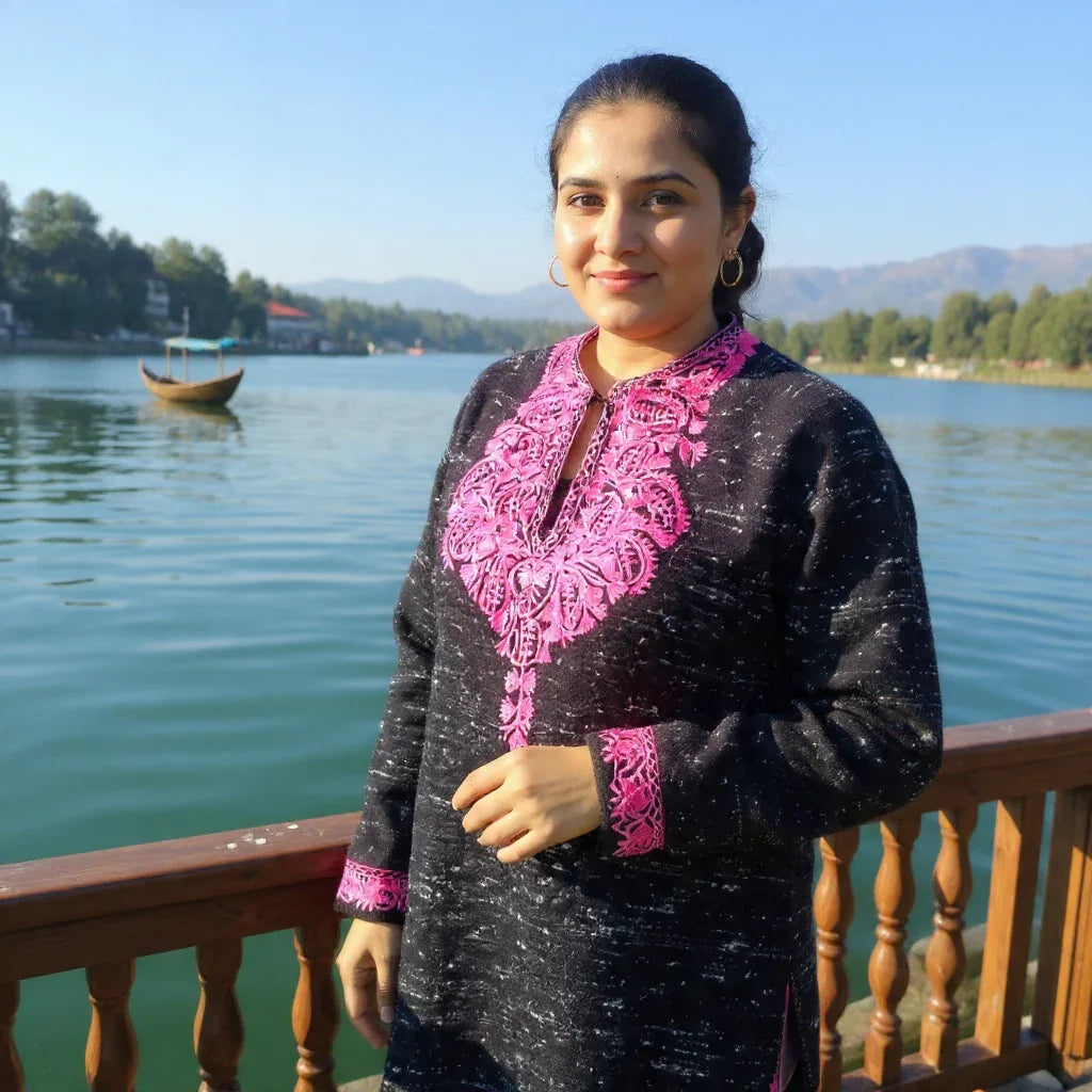 Woman wearing black woolen garment with pink embroidery by lake with wooden railing and boat