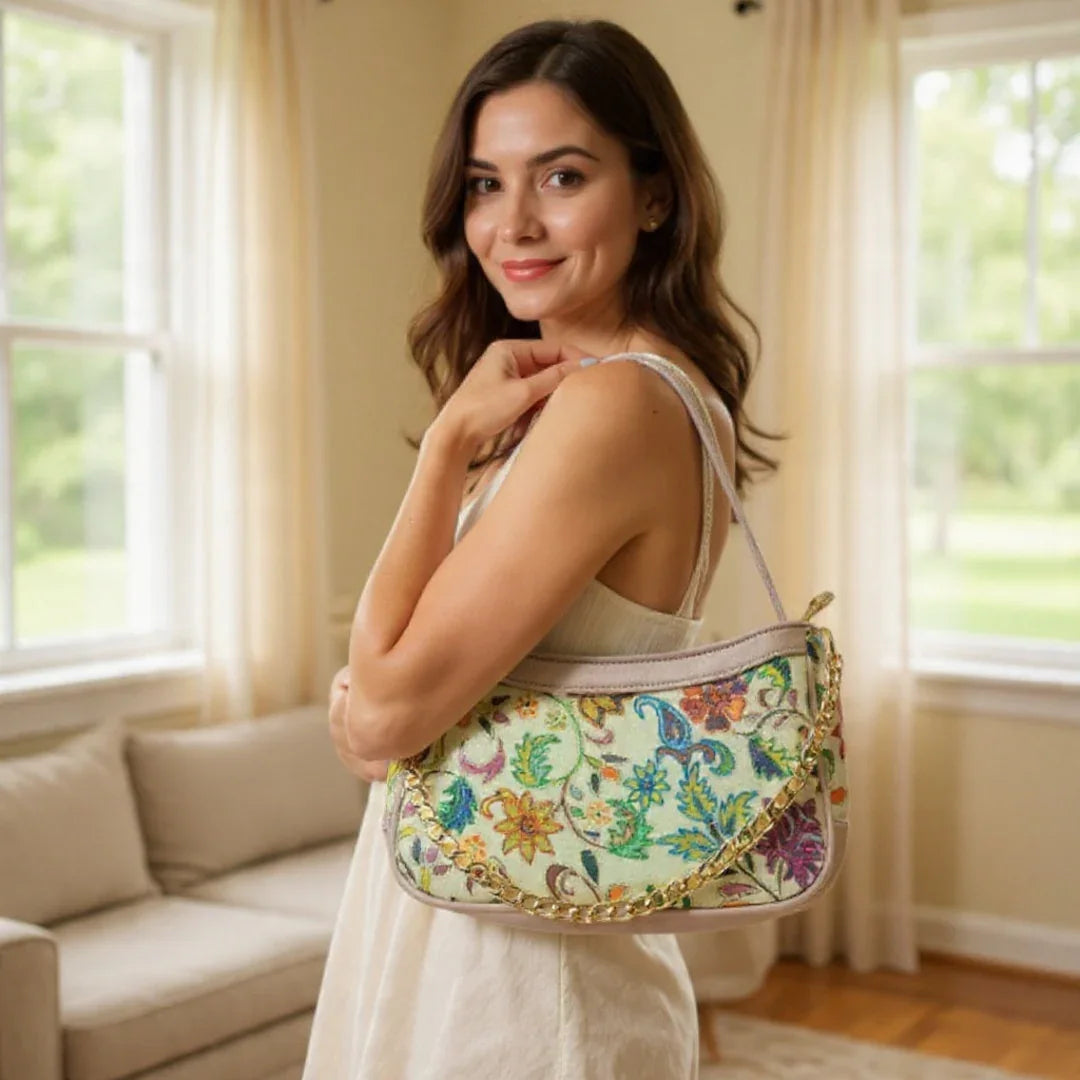 Woman indoors holding floral embroidered handbag with gold chain, near beige sofa and windows