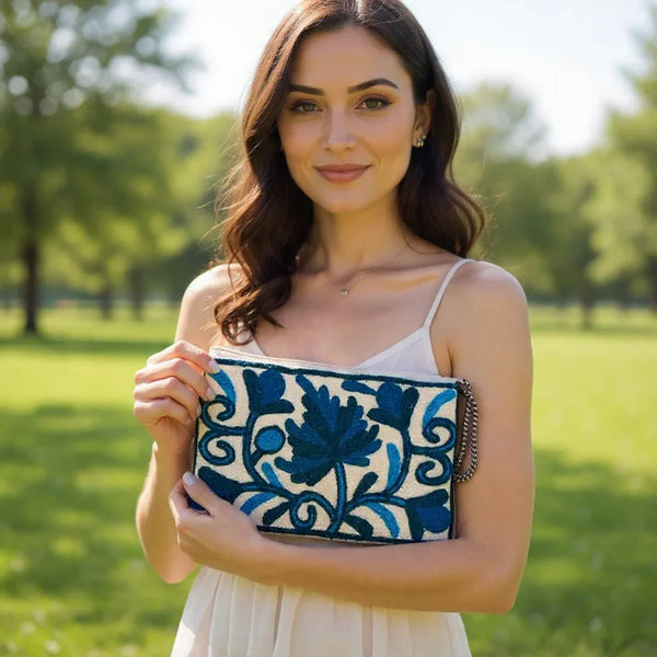 Woman in white dress holding handcrafted blue floral embroidered clutch outdoors in sunny park