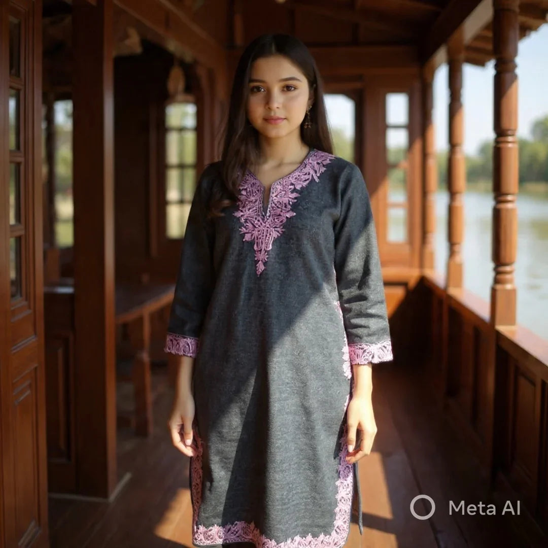 Woman wearing a gray dress with pink embroidery standing in a wooden verandah by the water at Zanskar Arts