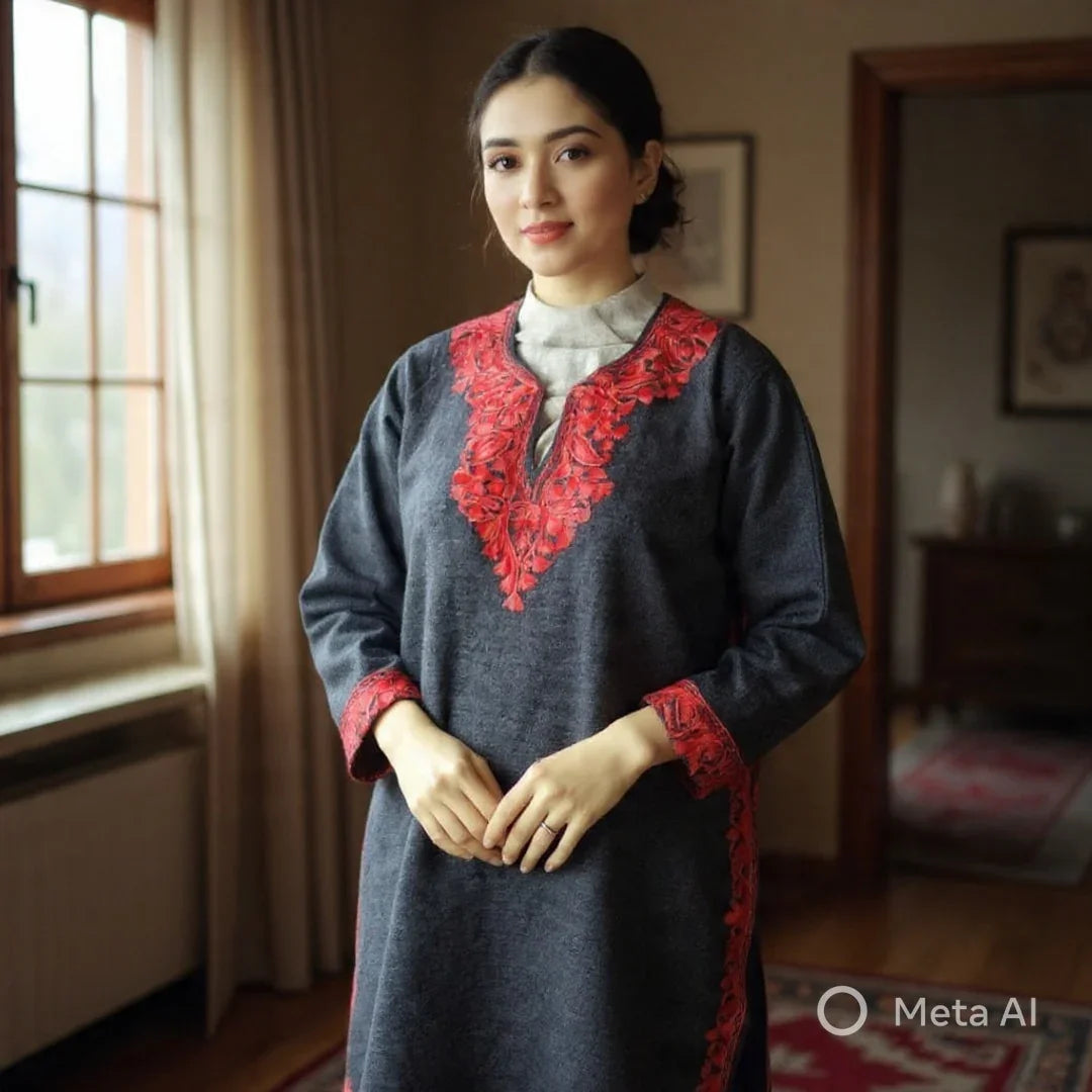Woman wearing a dark grey kurta with red floral embroidery on the neckline and cuffs, standing indoors near a window