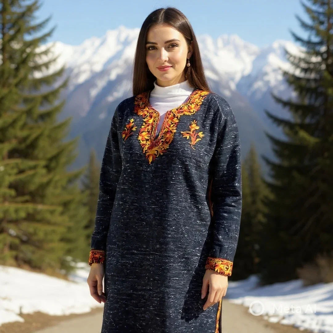 Woman wearing a dark blue embroidered woolen kurta with orange floral patterns, standing outdoors with snowy mountains and pine trees in the background, showcasing winter ethnic wear from Zanskar Arts