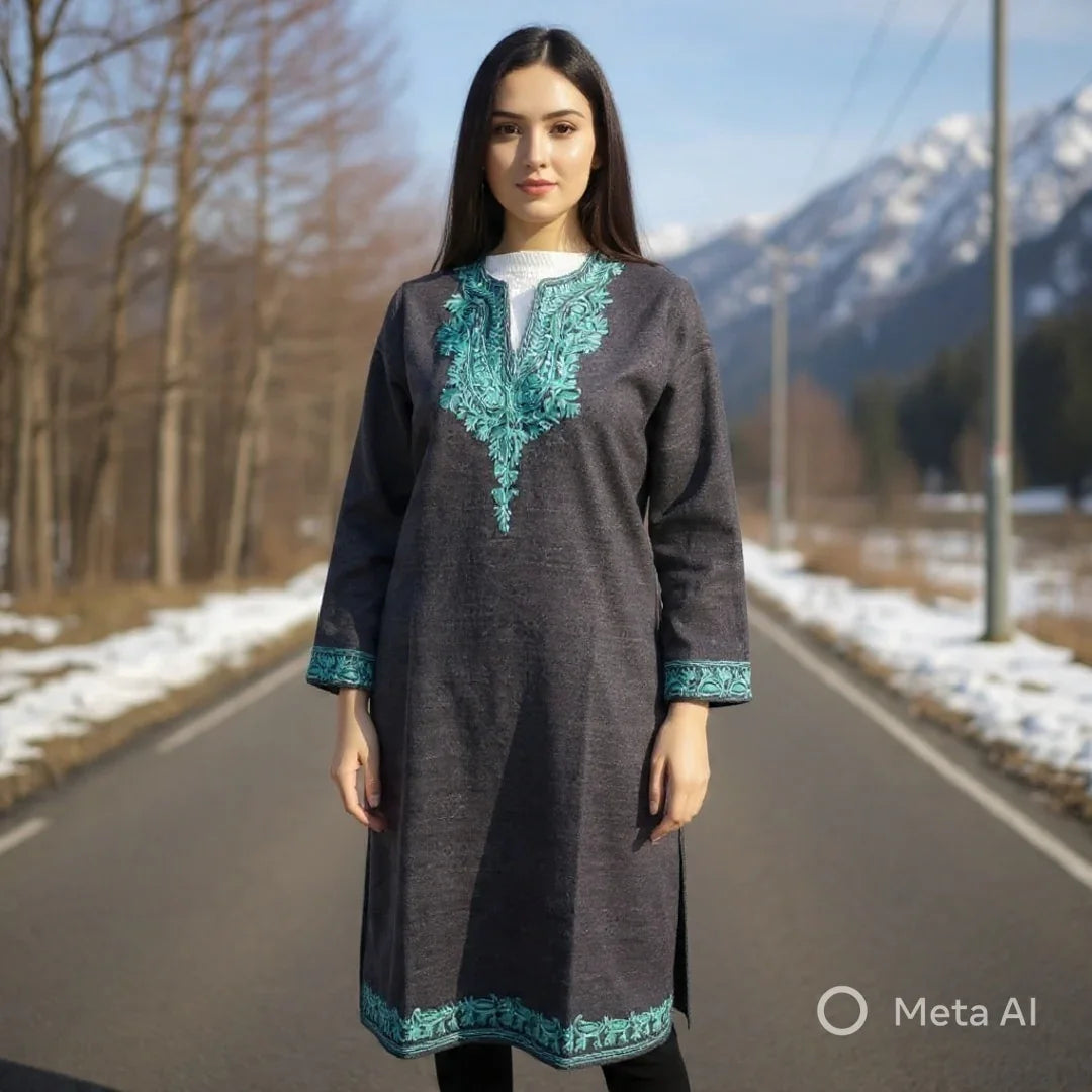 Woman wearing a dark grey pashmina shawl dress with teal embroidery standing on a snowy mountain road